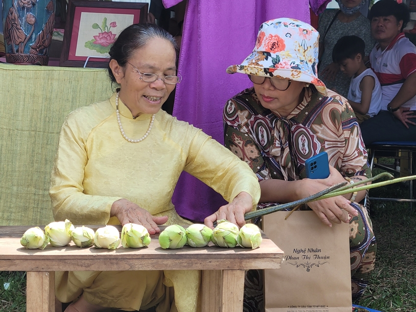 Nghệ nhân Phan Thị Thuận (bìa trái) thao diễn rút tơ sen dệt lụa phục vụ du khách tham quan tại Festival NTT Huế 2023 