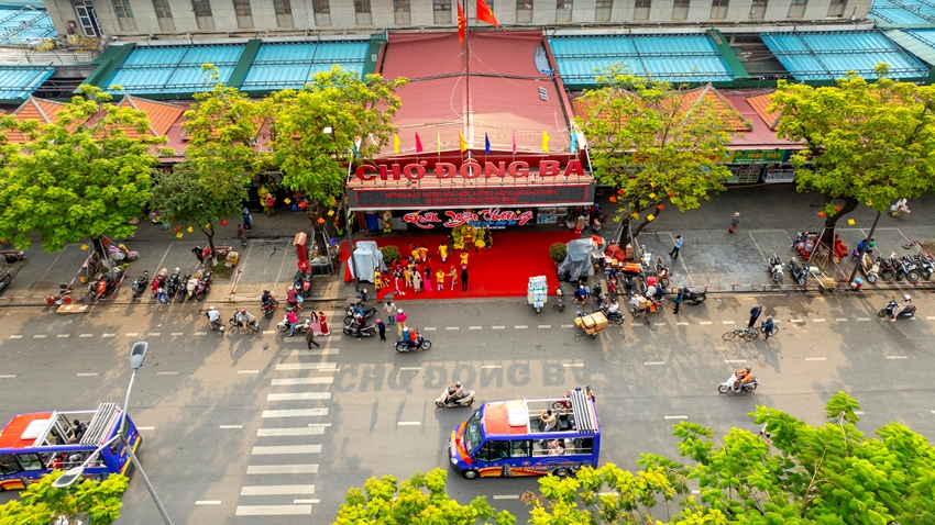 The open-top single-decker bus passes through Dong Ba Market, carrying passengers.